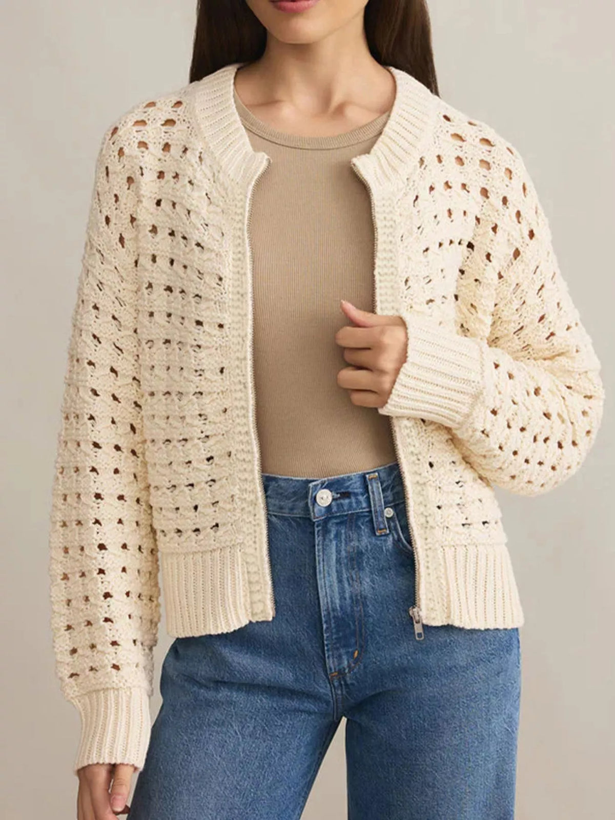 Beige openwork zip-up cardigan with ribbed cuffs and collar, styled with a tan top and jeans.