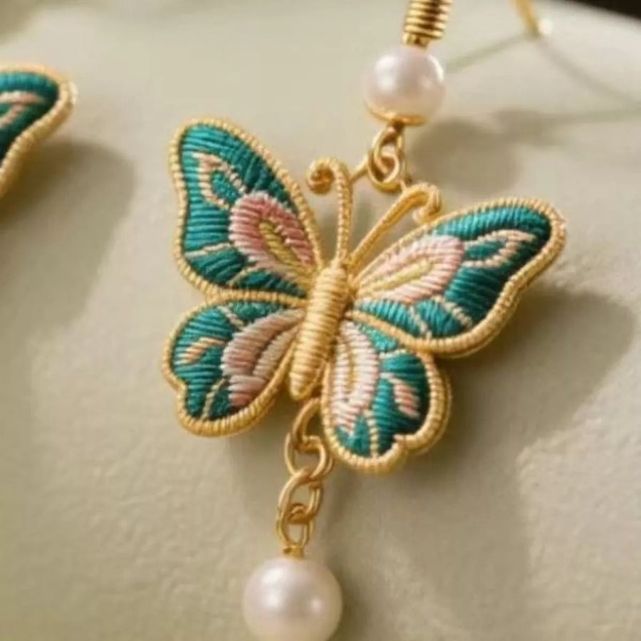 Gold butterfly dangle earrings with pearl drop and embroidered details.
