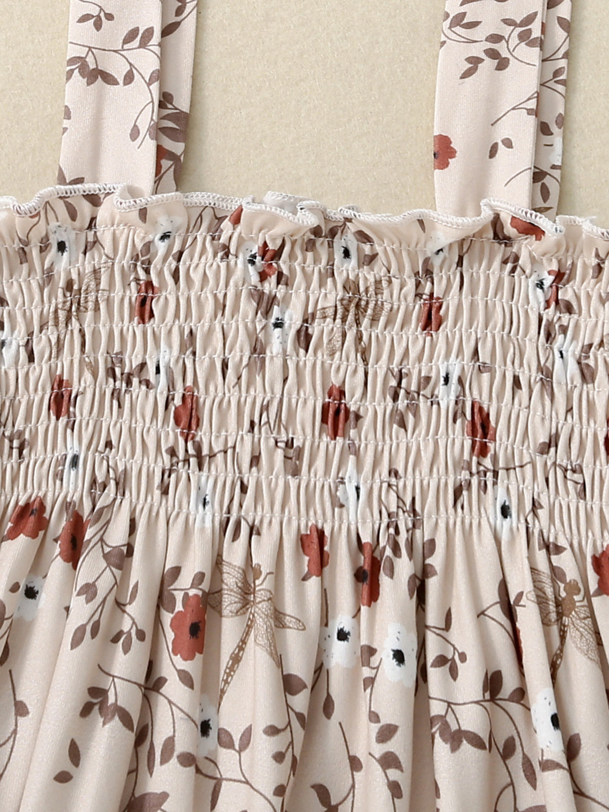 Baby jumpsuit with apricot floral print, smocked bodice, and ruffled neckline.