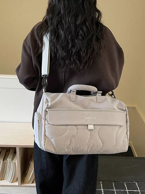 Luxurious quilted duffel bag in light gray with adjustable strap and front pocket.