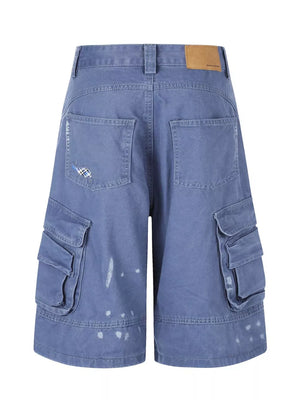 Blue faded cargo capris with distressed paint splatters and stylish patch detail.