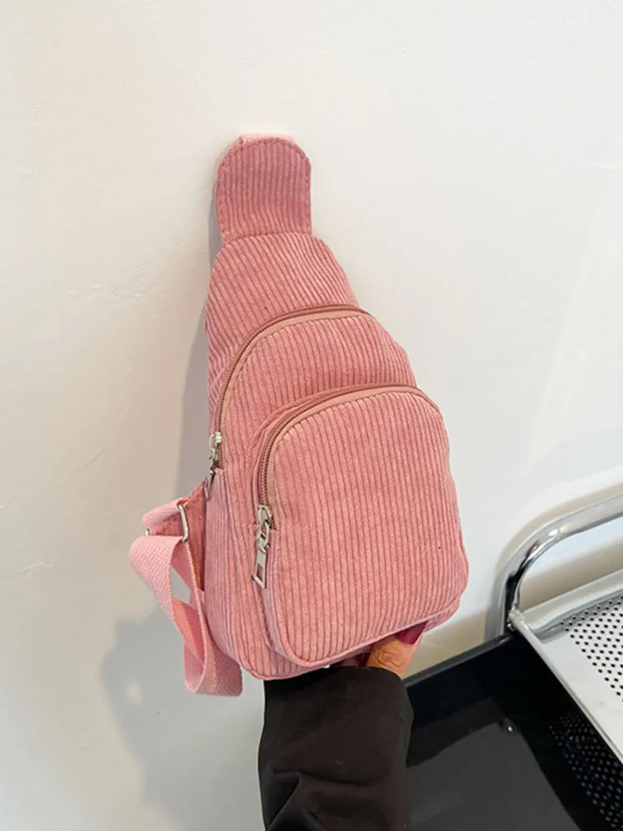 Pink corduroy sling bag with zip pockets and adjustable strap.