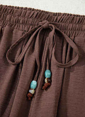 Brown relaxed wide-leg maternity pants with drawstring and beaded detail.
