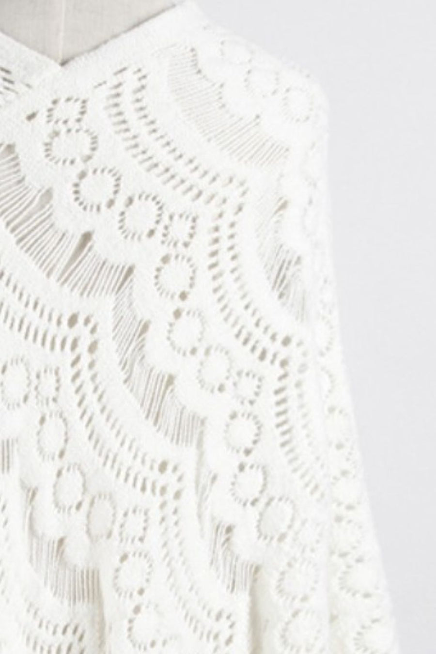 White crochet poncho with intricate openwork pattern and fringe detail.