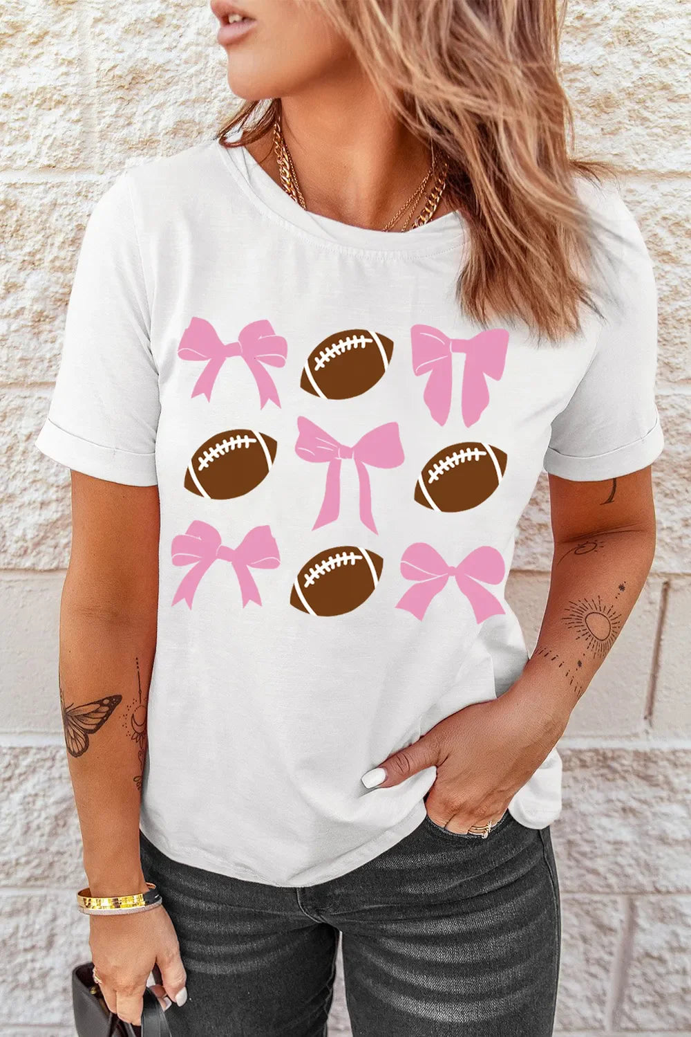 White t-shirt with a grid pattern of pink bows and brown footballs.