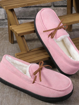 Pink suede moccasin slippers with faux fur lining and bow detail.
