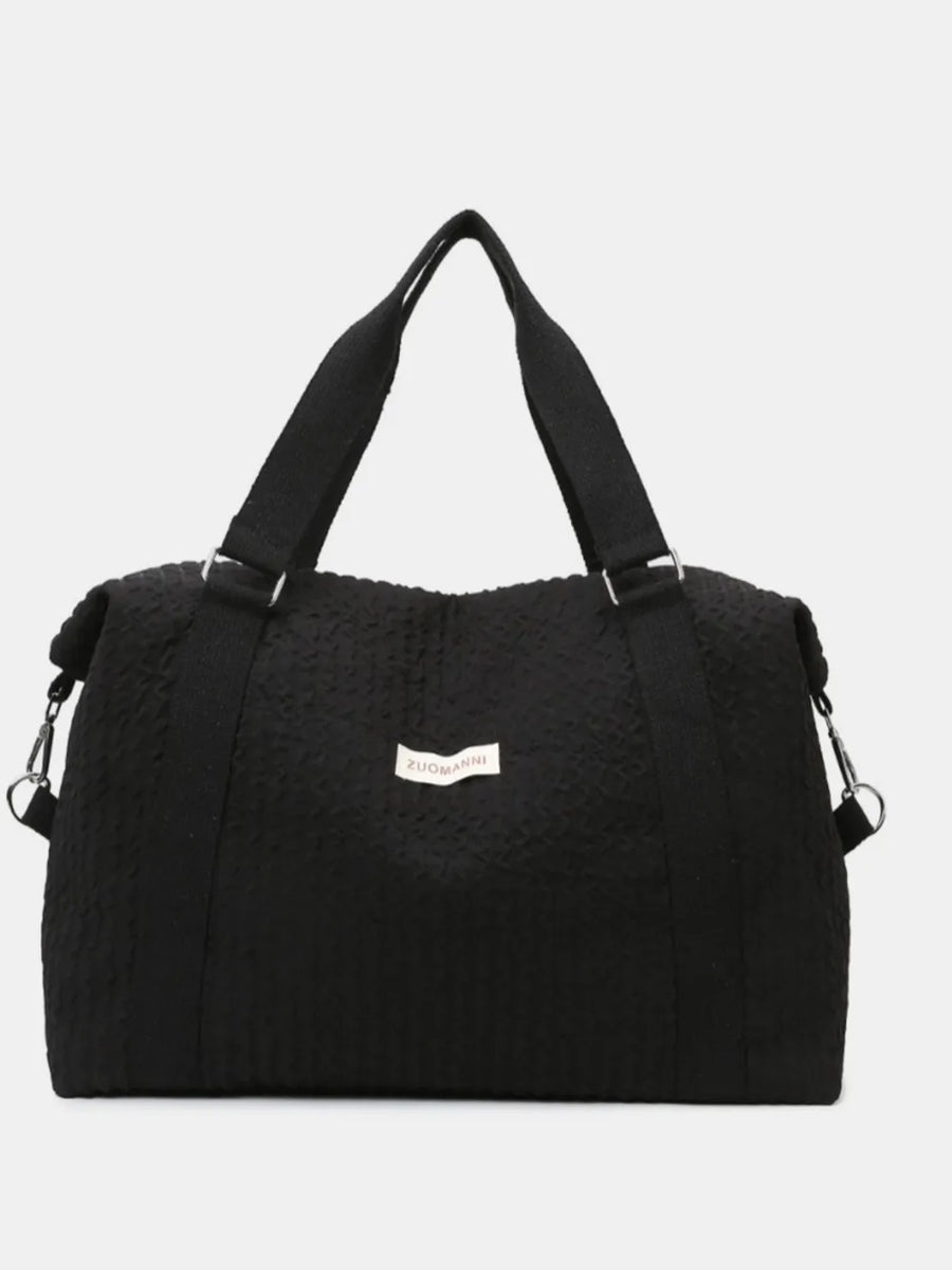 Black waffle-weave weekend bag with silver hardware and adjustable strap.
