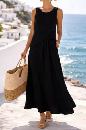 Black sleeveless maxi dress with contrast seam detail and pockets, styled with sandals and a straw tote.