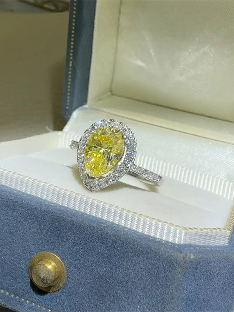 Yellow pear-cut moissanite ring with diamond halo in a jewelry box.