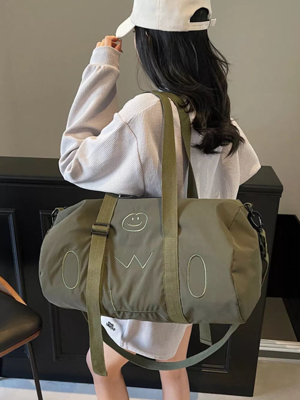 Green duffel bag with cheerful smiley face and abstract design, adjustable strap.