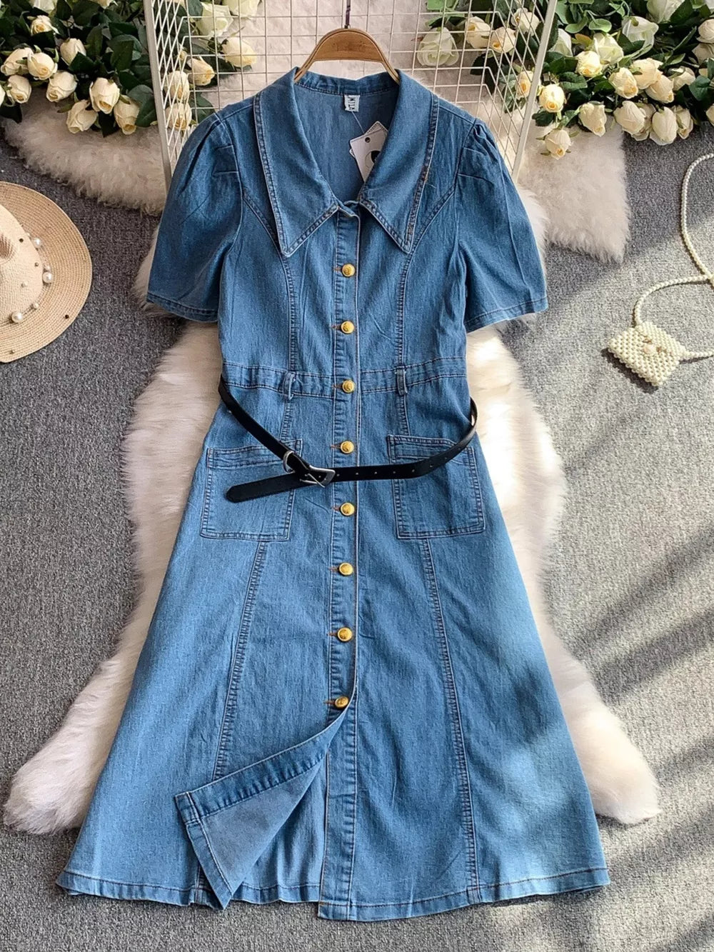 Light blue denim collared dress with short puff sleeves, gold buttons, and a black belted waist.