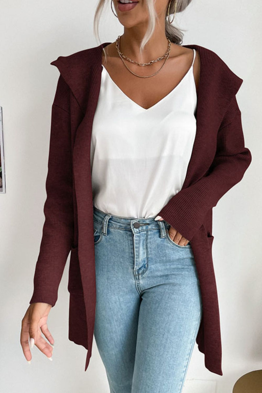 Burgundy ribbed knit hooded cardigan with drape front and pockets, worn open over a white cami and jeans.