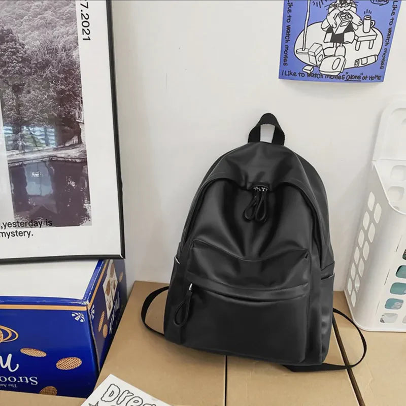 Black minimalist leather backpack with front zip pocket and dual zipper main compartment.