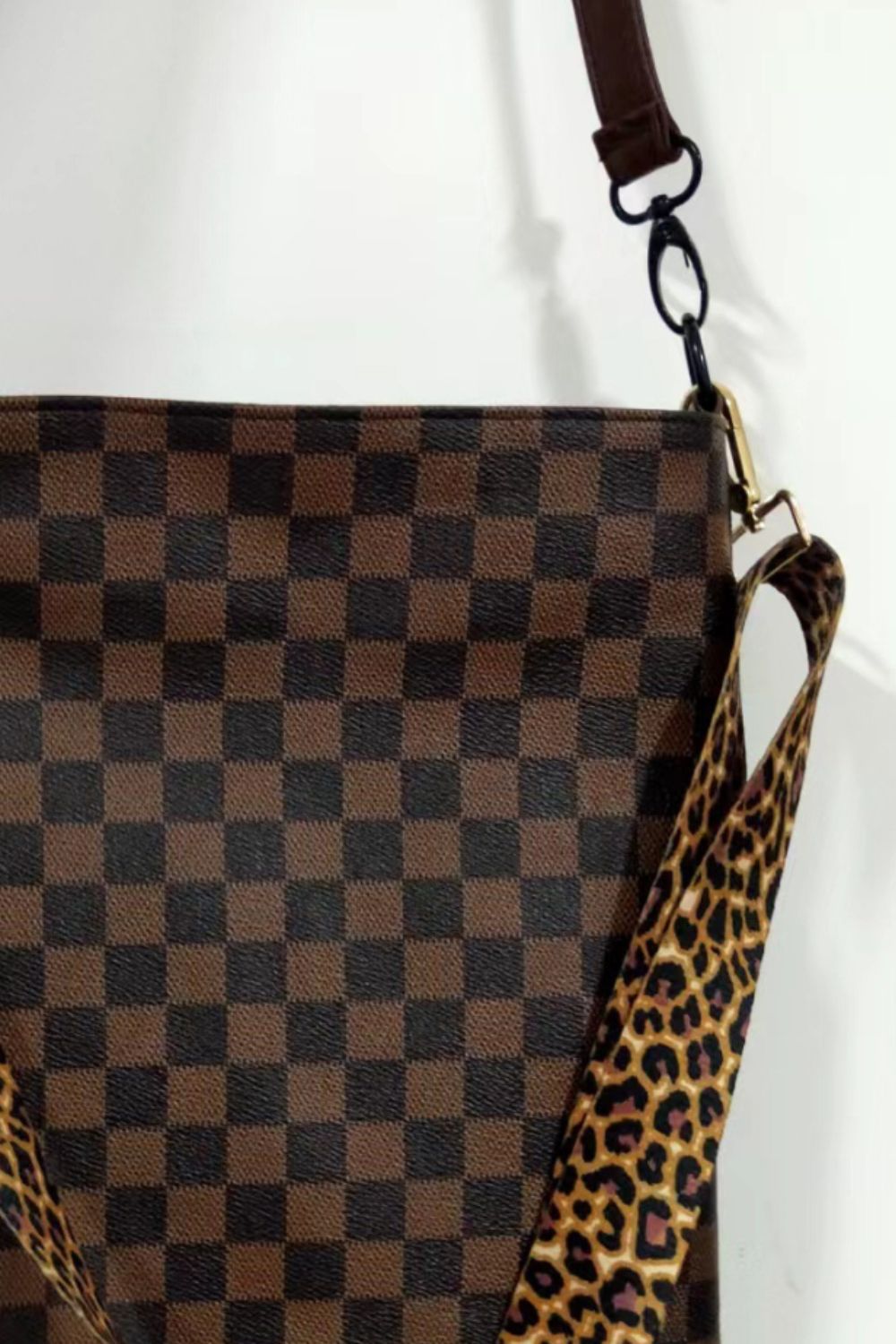 Chocolate checkered crossbody bag with leopard print strap and tassel detail.