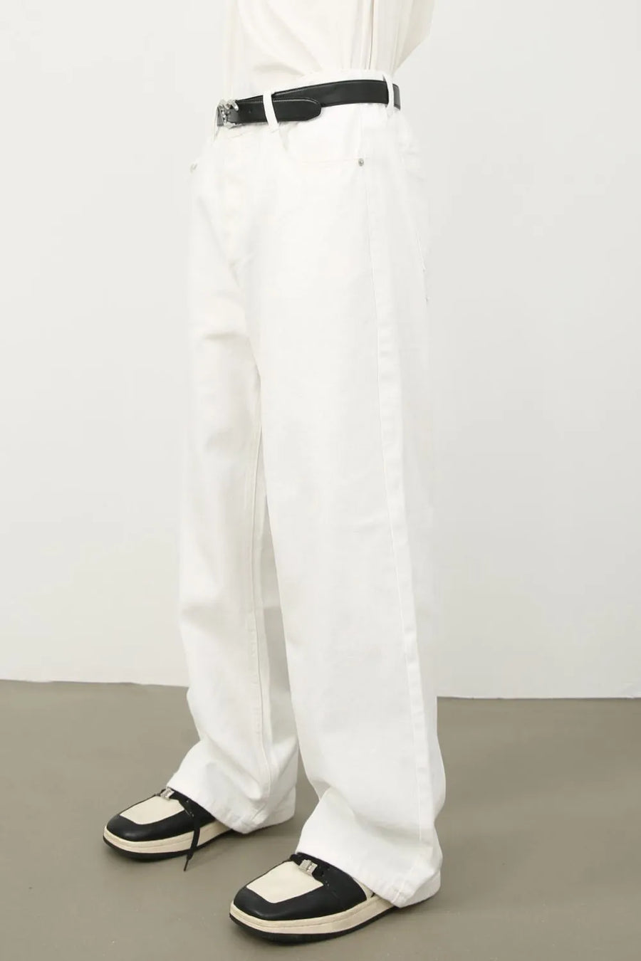 Sculpted wide leg ivory denim trousers with a black belt and two-tone sneakers.