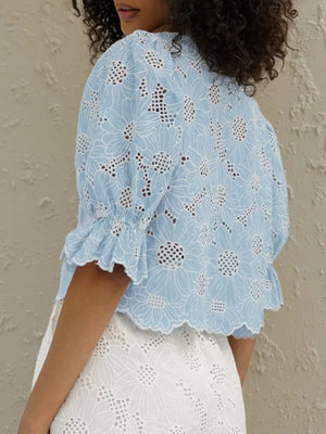 Blue eyelet crop top with white floral embroidery, ruffled short sleeves, and scalloped hem.