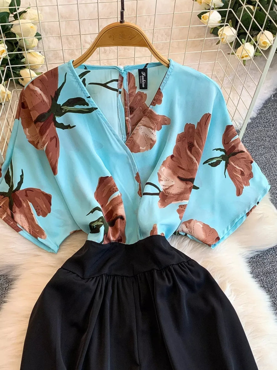 Blue abstract floral print wide-leg romper with black gathered waist and pockets.