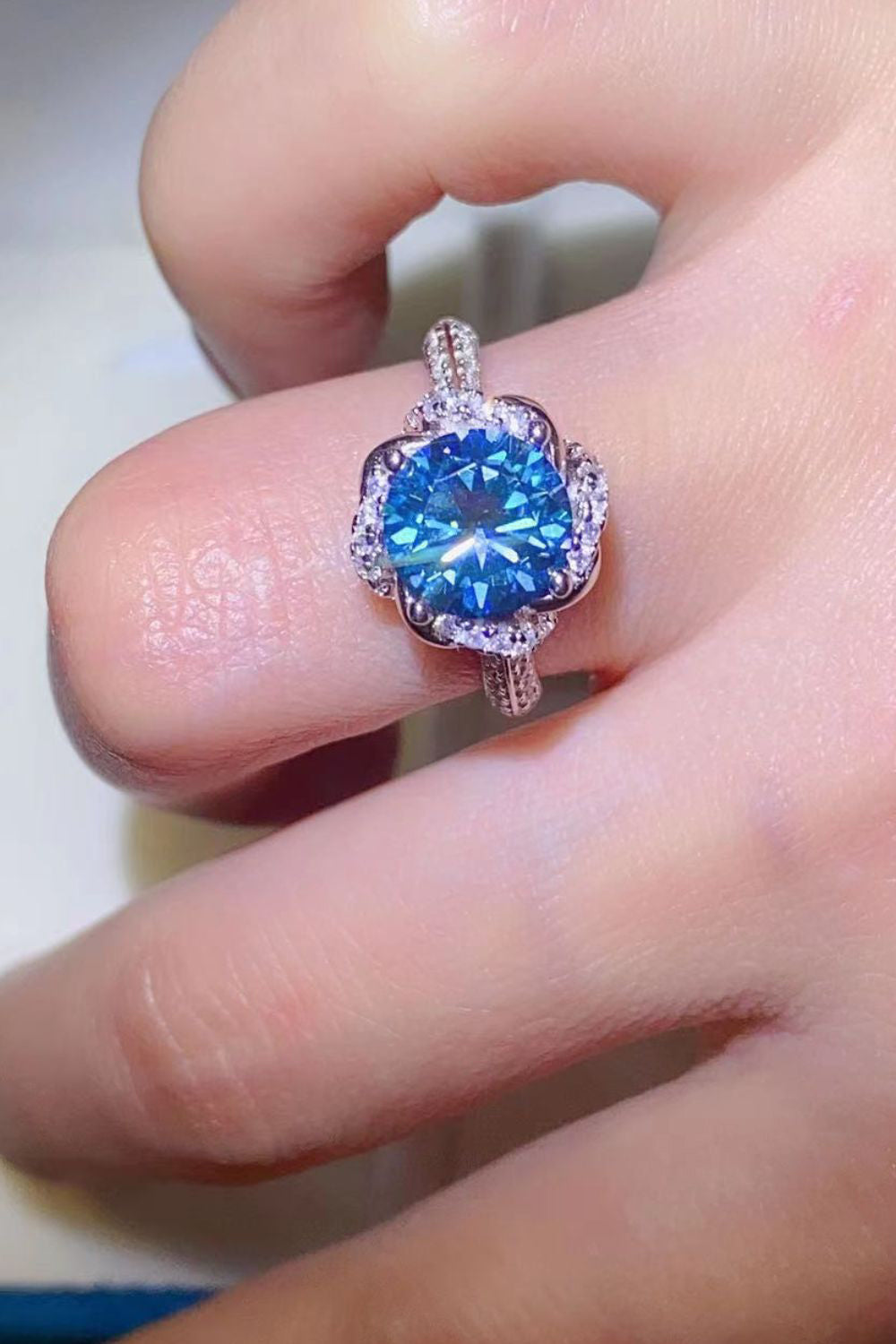 Blue moissanite halo ring with diamond accents on a hand