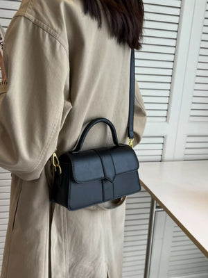 Chic small black top handle shoulder bag with gold hardware and a long strap.