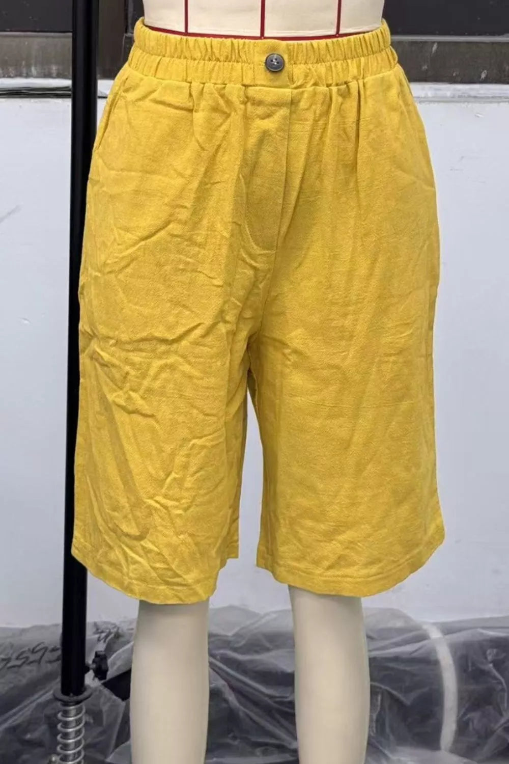 Mustard yellow pocketed knee-length denim shorts with elastic waistband and button closure.