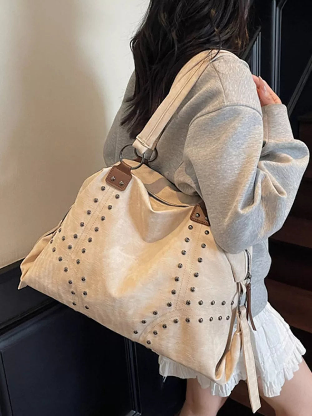 Cream white distressed studded trapezoid handbag with brown accents and fringe detail.