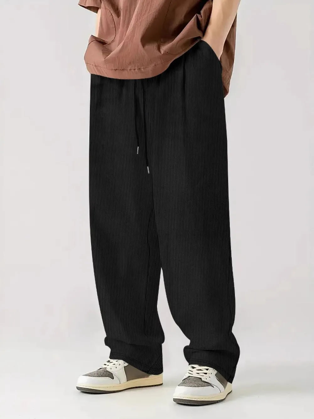 Black corduroy relaxed fit trousers with drawstring waist and vertical texture.