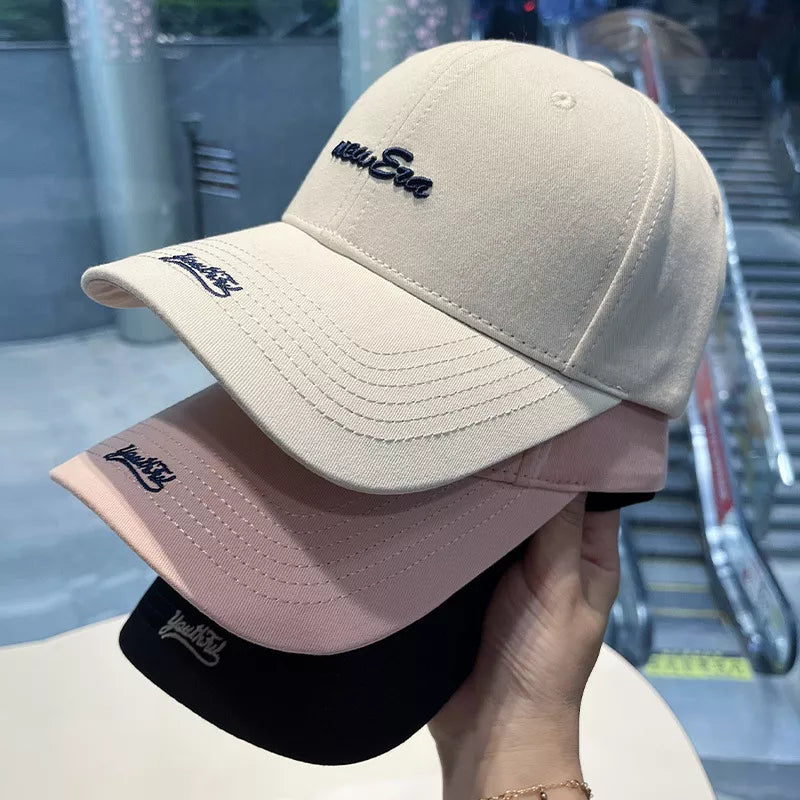 Embroidered baseball cap in off white, pink, and black with navy blue lettering.