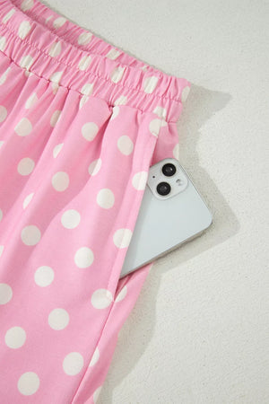 Pink polka dot polyester shorts with pockets and elastic waist, phone visible in pocket.