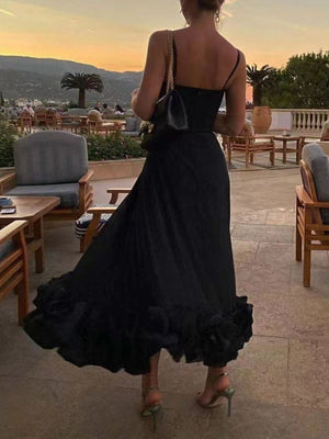 Black midi dress with spaghetti straps and a ruffled hem, styled with heels.
