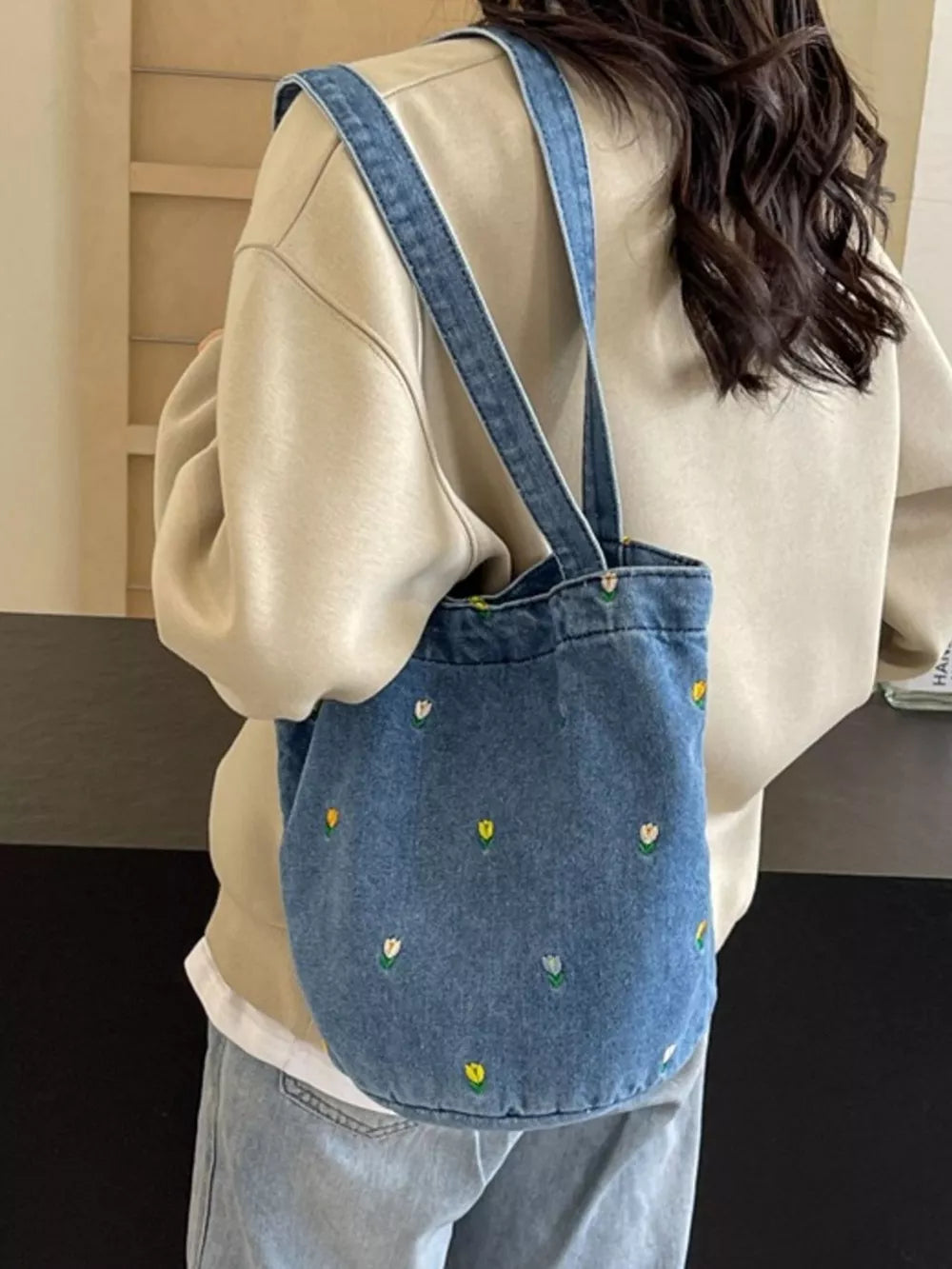 Denim tote bag with embroidered whimsical floral pattern and double straps.