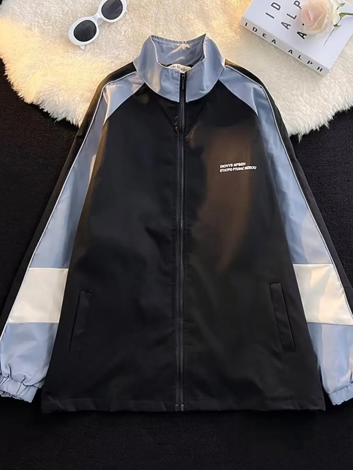 Men's black zip-up track jacket with blue and white colorblock sleeves and white text detail.