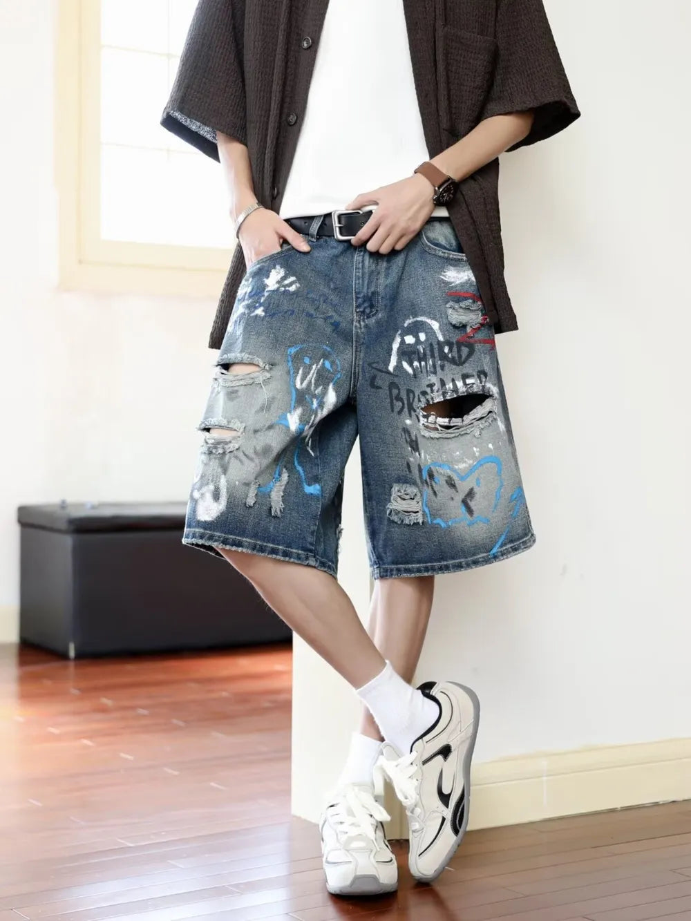 Men's distressed blue denim shorts with graffiti print and rips.