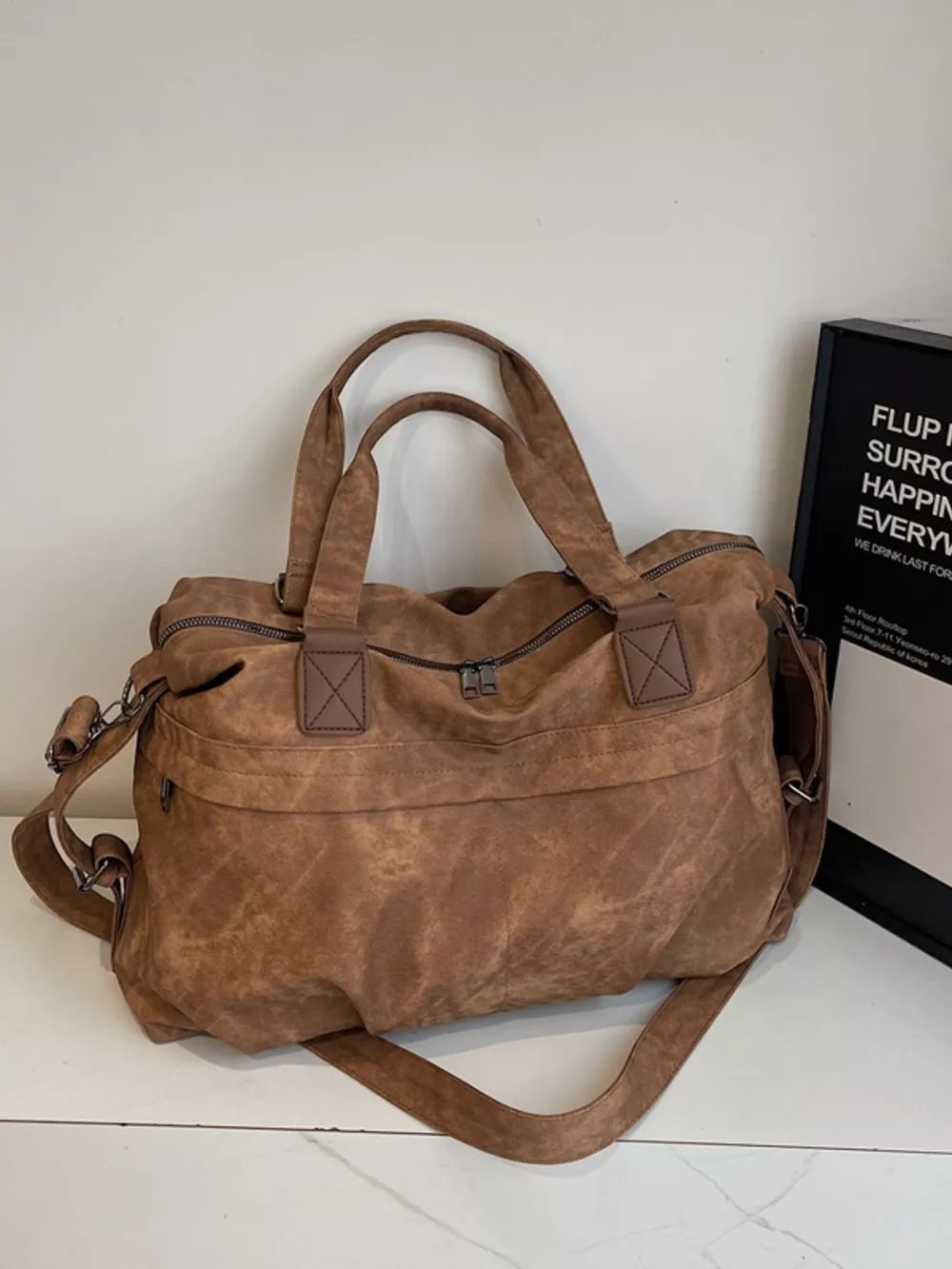 Brown suede duffel bag with double top handles and a detachable shoulder strap.