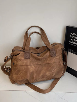Brown suede duffel bag with double top handles and a detachable shoulder strap.