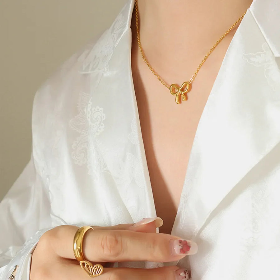 Delicate gold bow pendant necklace on a fine chain, styled with a white satin shirt.