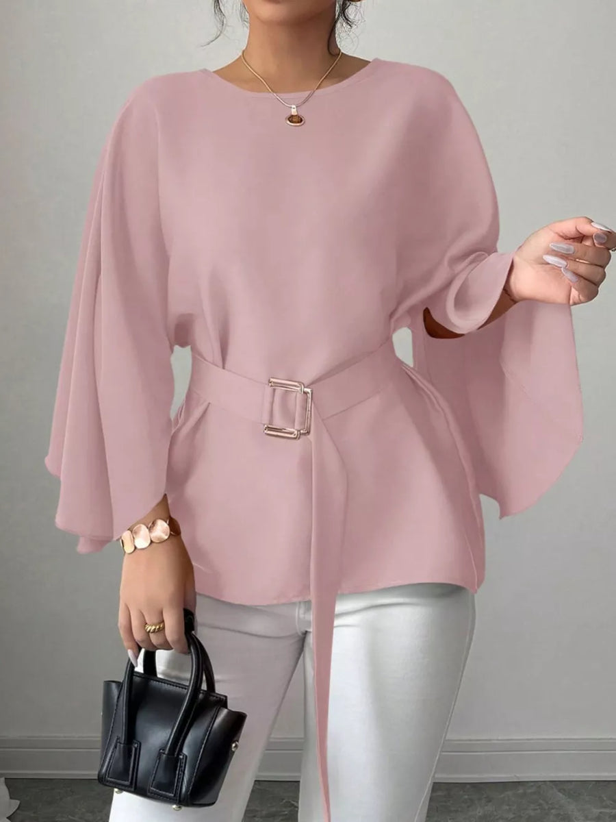 Pink belted blouse with batwing sleeves and a gold buckle, styled with white pants.