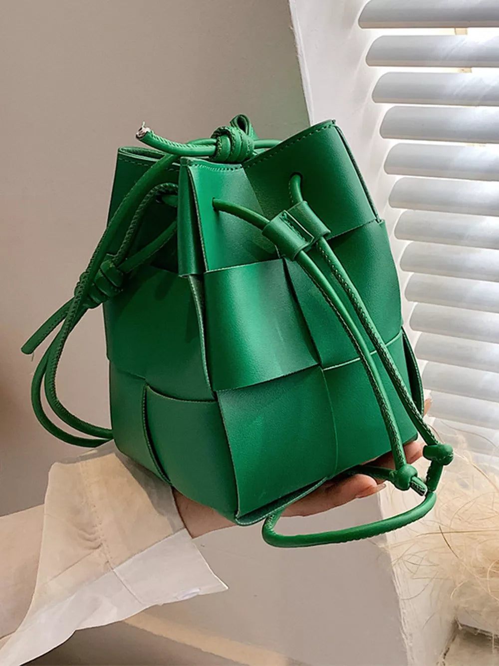 Green woven mini bucket bag with drawstring closure and braided strap detail.