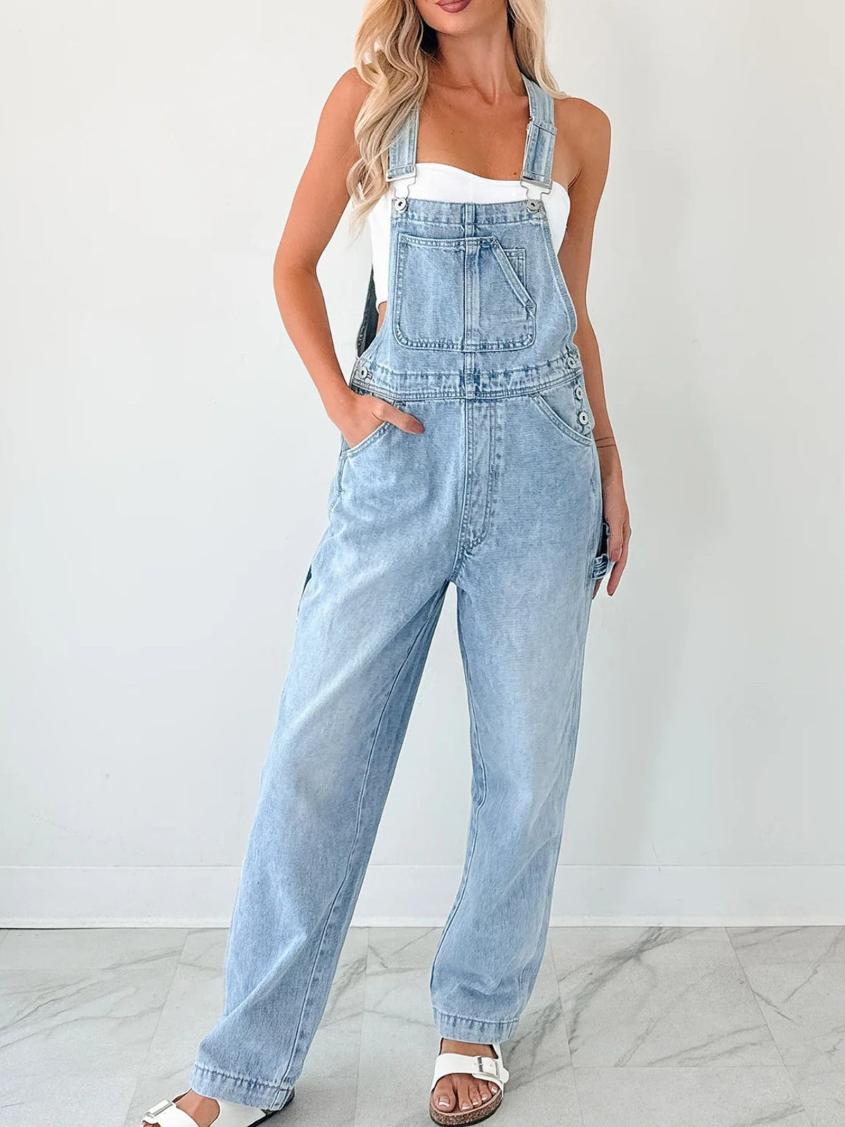 Light wash denim overalls with wide straps, bib pocket, and relaxed fit pants.