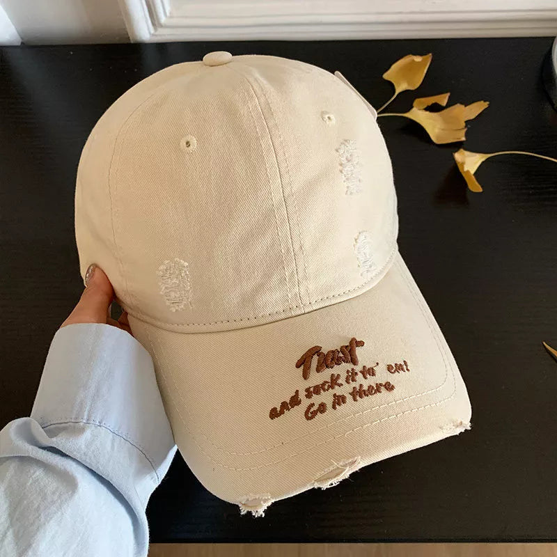 Beige distressed baseball cap with embroidered text and frayed brim.