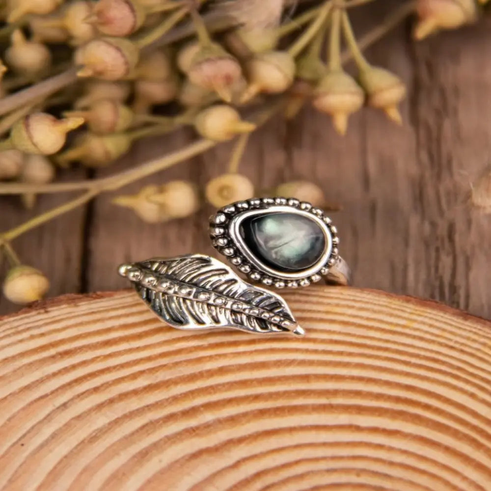 Silver bypass ring with a pearlescent oval stone and a detailed leaf design.
