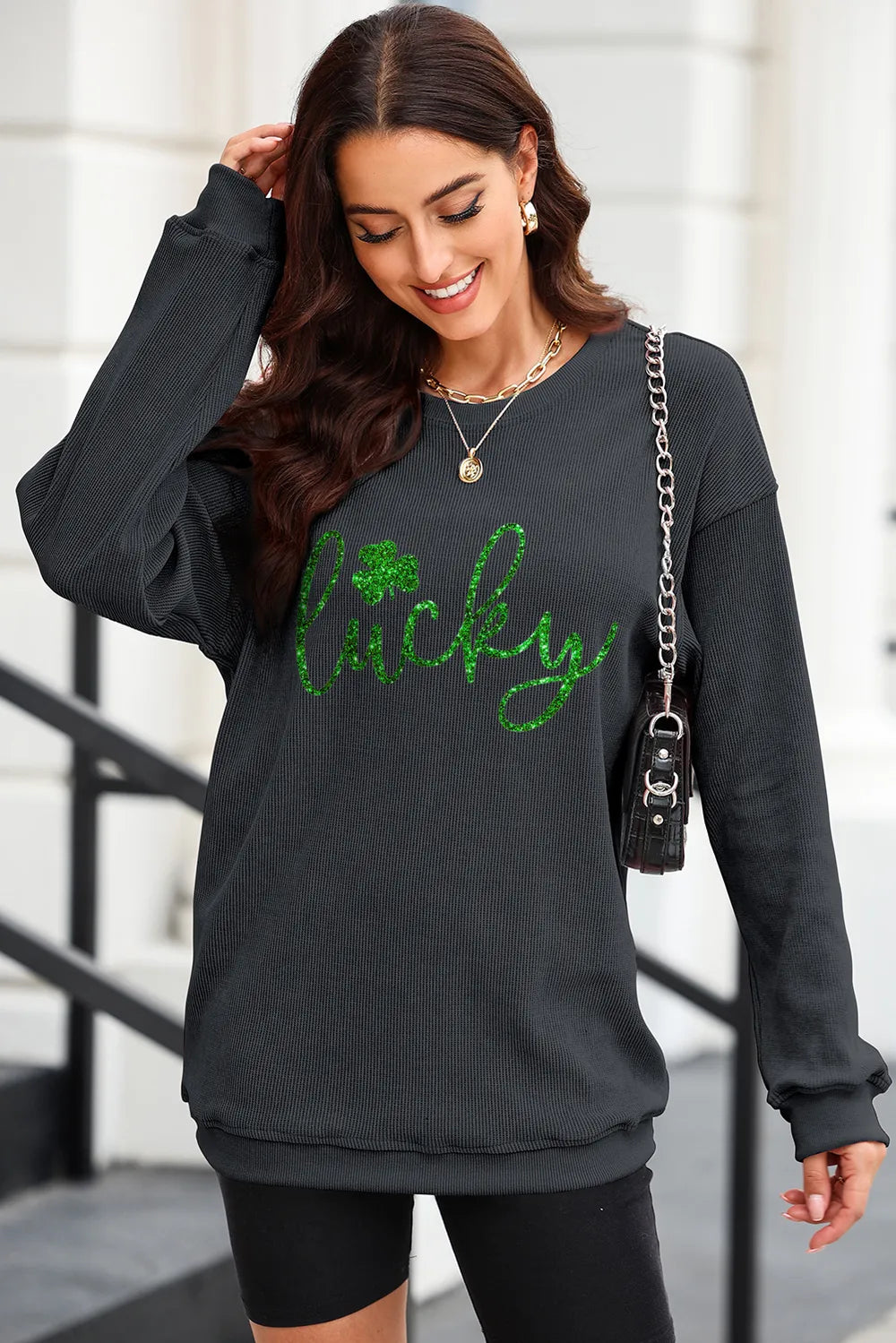 Black ribbed sweatshirt with green glitter "Lucky" graphic and shamrock detail.