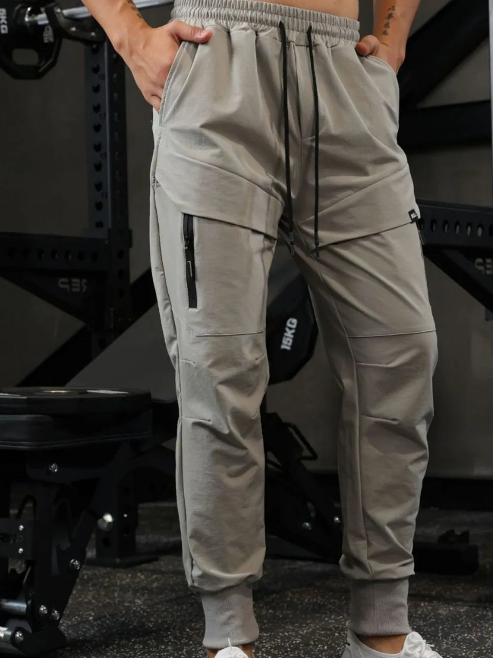 Gray technical joggers with zip cargo pockets and drawstring waist.