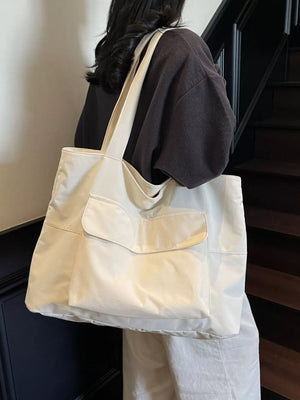 Spacious cream nylon shoulder bag with flap and exterior pockets, worn by a woman.