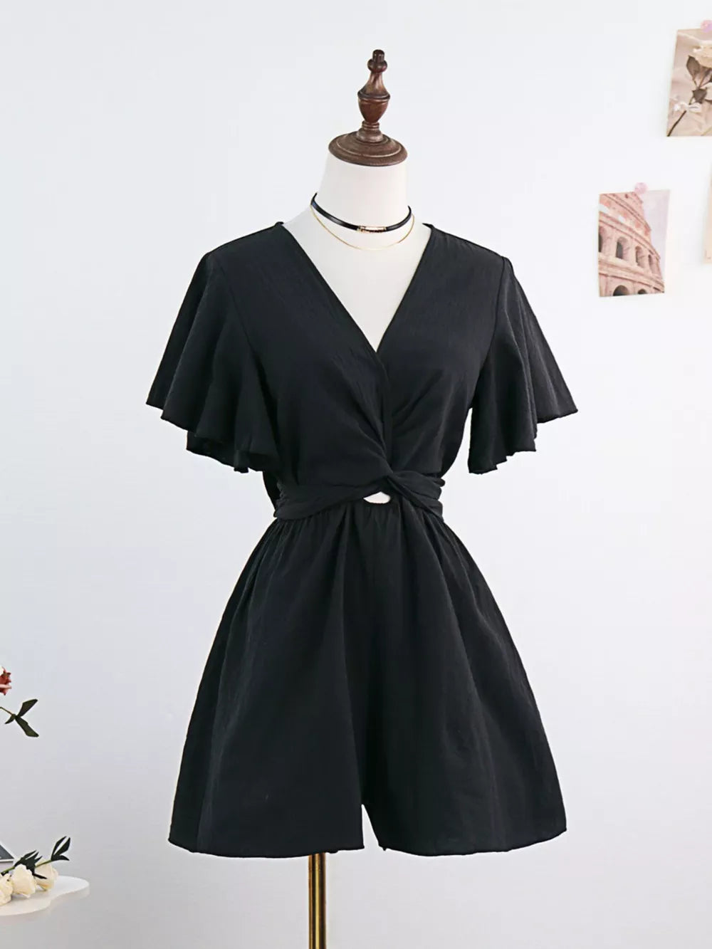 Black flutter sleeve tie-waist romper with V-neck and crisscross detail.