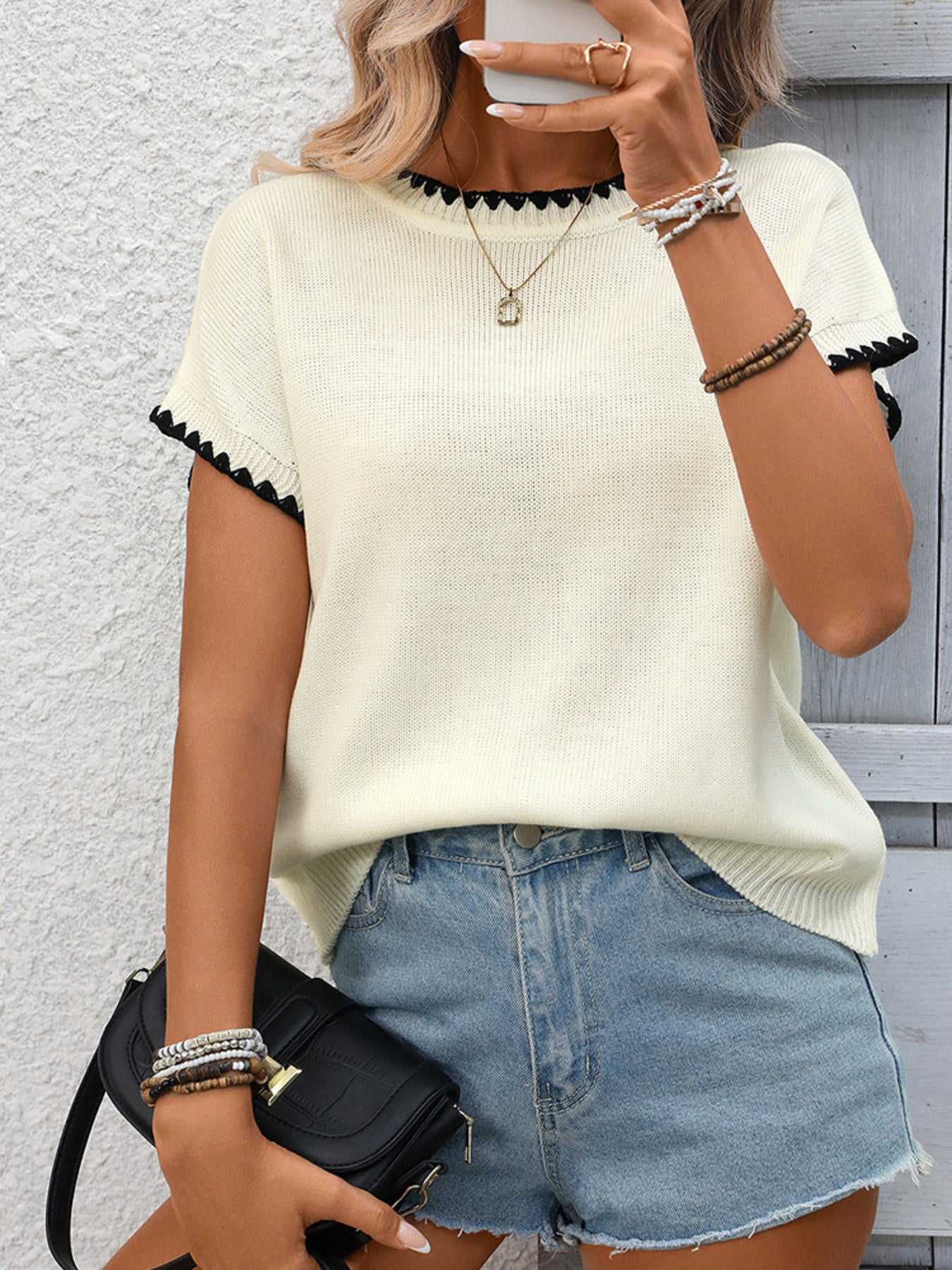 Off-white ribbed knit sweater with black contrast trim neckline and sleeves.