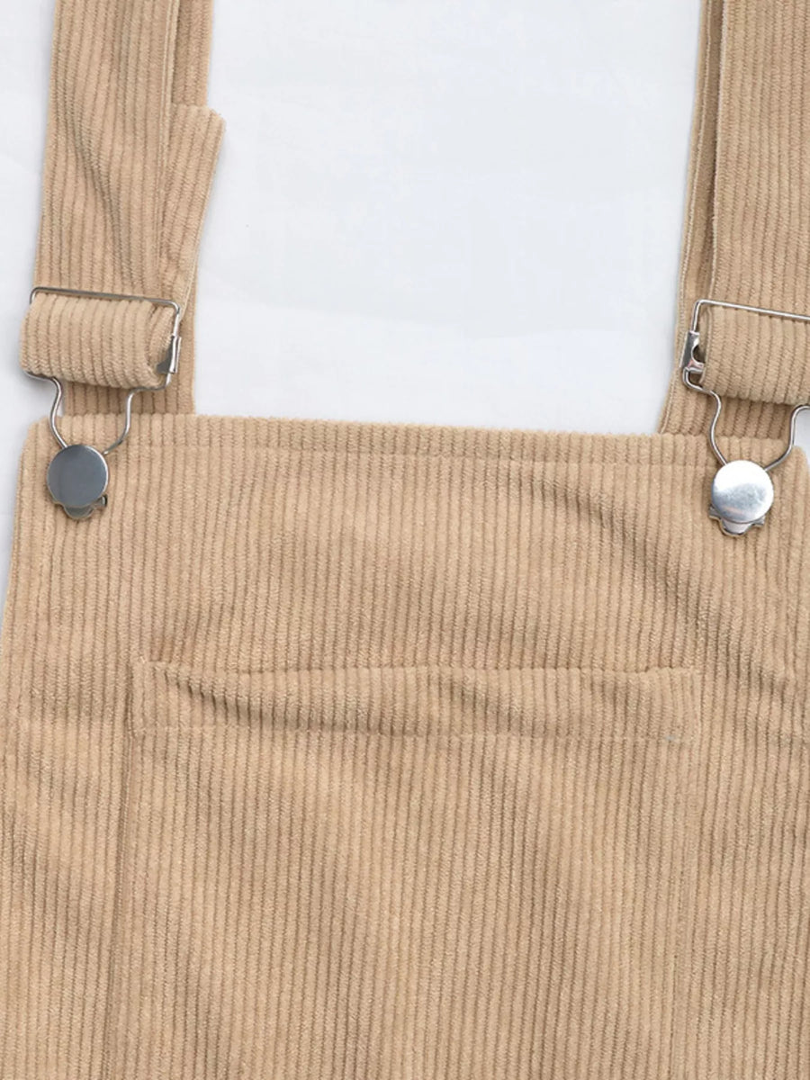 Tan corduroy overall dress with silver buckle straps and a front pocket.