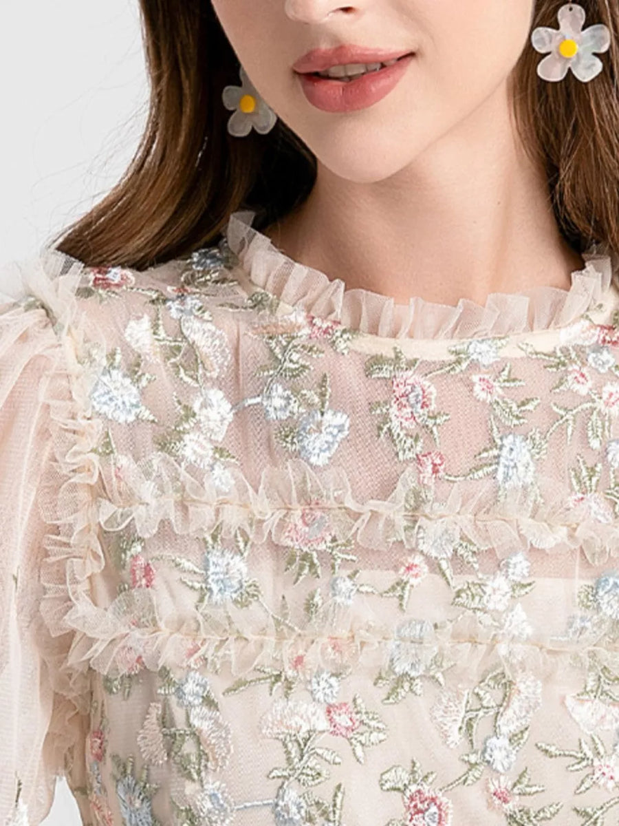 Embroidered floral tulle maxi gown with ruffled neckline and sleeves.