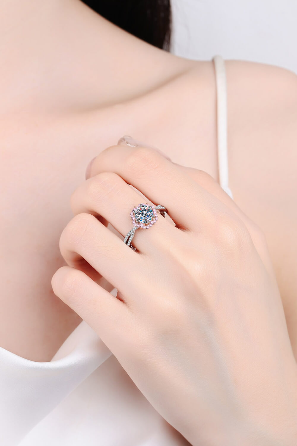 Silver moissanite ring with a round center stone and pink accent stones on a twisted band.