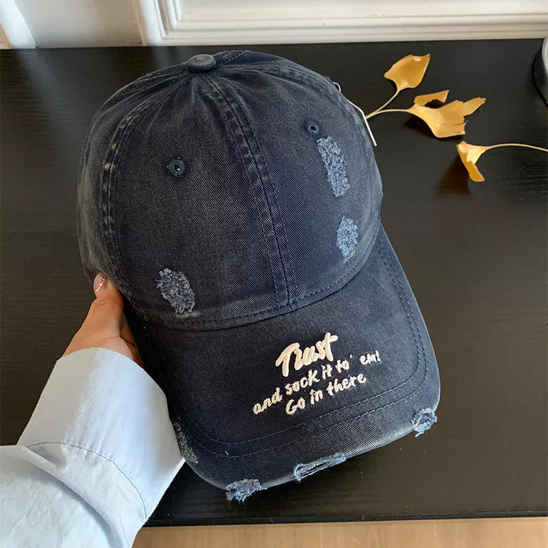 Distressed navy denim baseball cap with embroidered text and frayed details.