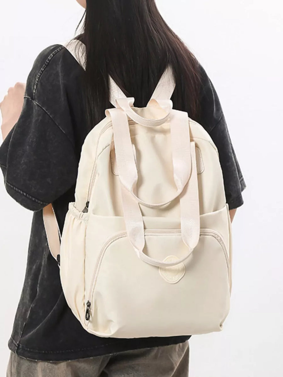 Off-white Oxford cloth backpack with adjustable straps and multiple pockets.
